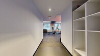 Located at 1 India St in Boston's historic waterfront neighborhood, this fitness center offers a well-appointed exercise space designed for efficient, focused workouts. The room features durable rubber tile flooring throughout, providing both safety and comfort underfoot. A striking dark textured ceiling contrasts with clean white walls, while linear LED lighting creates a modern, energetic atmosphere. Natural light filters in through street-facing windows, offering views of the surrounding Boston streetscape.

The space is thoughtfully organized to accommodate a range of workout types. Cardio equipment includes Life Fitness treadmills, an elliptical machine, and indoor cycling bikes positioned for easy use. A dedicated free weights area features a full dumbbell rack alongside a weight bench, catering to strength training needs. Wall-mounted flat-screen televisions are positioned throughout for entertainment during workouts. A large wall mirror enhances the sense of space and allows users to monitor their form. Additional amenities include a stability ball, battle ropes, and a mounted AED unit for safety. Built-in shelving near the entrance provides convenient storage. The overall ambiance is clean, functional, and contemporary, reflecting a professional fitness environment.