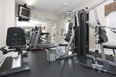 Located at 600 Ellen Way in Acworth, Georgia, this fitness center offers a well-equipped workout space designed to support a range of exercise routines. The single-floor facility features durable rubber flooring throughout, providing a safe and functional surface for both strength training and cardio activities.

The room is furnished with a multi-station strength machine by BATCA, a recumbent exercise bike, and a treadmill, offering users a comprehensive selection of equipment for varied fitness goals. A wall-mounted flat-screen television is positioned for easy viewing during workouts, adding convenience to longer training sessions. An exercise intensity reference chart is displayed on the wall, serving as a helpful guide for users monitoring their effort levels.

Full-length wall mirrors line one side of the room, visually expanding the space and allowing users to monitor their form during exercise. Overhead fluorescent lighting ensures the area is well-lit at all times. A door with a window provides access to the surrounding outdoor greenery, allowing natural light to filter into the space and offering views of the lush wooded landscape outside. A fire alarm is also present, reflecting attention to safety standards. The overall ambiance is clean, functional, and purpose-built to support an active lifestyle.