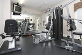 Located at 600 Ellen Way in Acworth, Georgia, this fitness center offers a well-equipped workout space designed to support a range of exercise routines. The single-floor facility features durable rubber flooring throughout, providing a safe and functional surface for both strength training and cardio activities.

The room is furnished with a multi-station strength machine by BATCA, a recumbent exercise bike, and a treadmill, offering users a comprehensive selection of equipment for varied fitness goals. A wall-mounted flat-screen television is positioned for easy viewing during workouts, adding convenience to longer training sessions. An exercise intensity reference chart is displayed on the wall, serving as a helpful guide for users monitoring their effort levels.

Full-length wall mirrors line one side of the room, visually expanding the space and allowing users to monitor their form during exercise. Overhead fluorescent lighting ensures the area is well-lit at all times. A door with a window provides access to the surrounding outdoor greenery, allowing natural light to filter into the space and offering views of the lush wooded landscape outside. A fire alarm is also present, reflecting attention to safety standards. The overall ambiance is clean, functional, and purpose-built to support an active lifestyle.