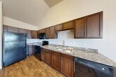 Located at 1431 Mike St, Unit 308, in Dickinson, North Dakota, this efficiently designed single-floor unit offers a practical and comfortable layout. The living area features plush wall-to-wall carpeting and is filled with natural light from two generously sized windows fitted with blinds, offering exterior views of the surrounding neighborhood. Baseboard heating runs along the perimeter, ensuring year-round comfort.

The kitchen is a functional and well-appointed space, featuring rich dark wood cabinetry that extends to the upper reaches of the vaulted ceiling, maximizing storage capacity. Granite-patterned countertops provide ample workspace, and the kitchen is fully equipped with black appliances, including a refrigerator, electric range, microwave, and dishwasher. Warm hardwood-style flooring runs throughout the kitchen, adding a cohesive and inviting feel.

The unit includes two bathrooms, both finished with consistent design elements. The vanity areas feature granite-patterned countertops, dark wood cabinetry, and large mirrors with overhead lighting. One bathroom includes a walk-in shower with a clean white surround, complemented by the same warm hardwood-style flooring that carries through the space. The overall ambiance is clean, neutral, and move-in ready.