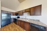 Located at 1431 Mike St, Unit 308, in Dickinson, North Dakota, this efficiently designed single-floor unit offers a practical and comfortable layout. The living area features plush wall-to-wall carpeting and is filled with natural light from two generously sized windows fitted with blinds, offering exterior views of the surrounding neighborhood. Baseboard heating runs along the perimeter, ensuring year-round comfort.

The kitchen is a functional and well-appointed space, featuring rich dark wood cabinetry that extends to the upper reaches of the vaulted ceiling, maximizing storage capacity. Granite-patterned countertops provide ample workspace, and the kitchen is fully equipped with black appliances, including a refrigerator, electric range, microwave, and dishwasher. Warm hardwood-style flooring runs throughout the kitchen, adding a cohesive and inviting feel.

The unit includes two bathrooms, both finished with consistent design elements. The vanity areas feature granite-patterned countertops, dark wood cabinetry, and large mirrors with overhead lighting. One bathroom includes a walk-in shower with a clean white surround, complemented by the same warm hardwood-style flooring that carries through the space. The overall ambiance is clean, neutral, and move-in ready.