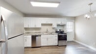 This two-story residence offers a clean, modern aesthetic with thoughtfully updated finishes throughout. The main level features a bright, open layout with durable hardwood-style flooring that flows seamlessly from the living area into the kitchen. The kitchen is well-equipped with crisp white shaker cabinets, granite-look countertops, a stainless steel dishwasher, range, and refrigerator, all illuminated by a large skylight overhead and accented by a stylish chandelier. A convenient exterior door provides direct access from the kitchen. The living area is open and airy, with a carpeted staircase leading to the upper floor. A full bathroom on the main level includes a white vanity and tub-shower combo, finished with wood-look flooring. Upstairs, two well-sized bedrooms each feature plush wall-to-wall carpeting, ceiling fans with integrated lighting, and windows that invite natural light. An additional bathroom upstairs mirrors the clean, neutral palette of the home, with a white vanity and soft, muted wall tones. Throughout the residence, warm beige walls, white trim, and consistent flooring choices create a cohesive and inviting atmosphere ideal for comfortable everyday living.
