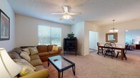 This single-floor residence offers a thoughtfully designed layout that balances comfort and functionality throughout its interconnected living spaces. The living room serves as a welcoming central hub, featuring plush wall-to-wall carpeting, a ceiling fan with integrated light fixture, and a large window fitted with horizontal blinds that fill the room with natural light and offer views of surrounding greenery. The space flows naturally into a dedicated dining area, which is anchored by a wooden table with seating for four and illuminated by an elegant pendant chandelier overhead.

The kitchen is well-equipped with white cabinetry, dark granite-style countertops, and white appliances including a refrigerator, electric range, and built-in microwave. A peninsula with bar stool seating connects the kitchen to the adjoining area, while hardwood flooring adds warmth and durability. A pantry with built-in shelving provides generous storage.

The bedroom is generously sized with soft carpeting, a ceiling fan, windows allowing natural light, and direct access to a spacious walk-in closet. The full bathroom features white cabinetry, a dark countertop vanity with a large mirror, a tub-shower combination, and bright overhead lighting.