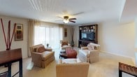 This single-floor residence offers a thoughtfully designed layout with a range of functional and comfortable living spaces. The living room serves as the heart of the home, featuring plush carpeting, a ceiling fan with light fixture, and a large sliding glass door that fills the room with natural light and provides access to an outdoor area. A built-in entertainment center anchors the room, complemented by ample seating space. The galley-style kitchen is efficiently arranged with rich dark cabinetry, light countertops, recessed lighting, stainless steel appliances including a built-in microwave, and a dedicated walk-in pantry offering generous storage. The bedroom is a serene retreat with soft carpet, a ceiling fan, and windows that allow natural light to filter in. It is accompanied by a closet with louvered bi-fold doors and convenient access to the bathroom. The bathroom is clean and classic, featuring a full tub-and-shower combination with a curved curtain rod, a toilet, and a large vanity mirror. Throughout the residence, a warm, neutral color palette and consistent design choices create a cohesive and inviting ambiance suited for comfortable everyday living.