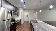 Located at 2025 Barrett Lakes Blvd NW in Kennesaw, GA, this well-appointed 2-bedroom, 2-bathroom residence offers a thoughtfully designed single-floor layout. The open-concept kitchen and living area serves as the heart of the home, featuring rich dark cabinetry, granite countertops, a center island with a built-in sink, stainless steel appliances including a refrigerator, electric range, and microwave, plus a tile backsplash. Track lighting and elegant pendant lights illuminate the kitchen, while the adjacent living room benefits from natural light through large windows and is finished with gleaming hardwood-style flooring and crown molding. The spacious primary bedroom includes a ceiling fan and connects to its own bathroom. The second bedroom is carpeted and receives ample natural light with views of the surrounding greenery. Both bathrooms are finished with granite-topped vanities and clean white tile, with one featuring a soaking tub and shower combo. Additional highlights include two closets and a dedicated in-unit laundry area. The neutral color palette and consistent finishes throughout create a cohesive, move-in-ready atmosphere.