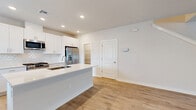 This two-story home is designed for comfortable, functional living across two well-proportioned floors. The main level features an open-concept layout that seamlessly integrates the living room, dining area, and kitchen into one cohesive space. The living room is bright and welcoming, finished with light hardwood-style flooring and a ceiling fan, while natural light filters in through multiple windows. The kitchen stands out with crisp white shaker cabinetry, a large center island with an undermount sink and quartz countertop, stainless steel appliances including a gas range, microwave, and French door refrigerator, and recessed lighting. A pantry provides additional storage. The main floor also includes a garage with an automatic opener and a dedicated laundry area. Upstairs, the second floor houses all three bedrooms, each carpeted and served by generous closet space — with six closets distributed throughout the home. The spacious primary bedroom offers its own private bathroom. Three additional bathrooms feature clean, bright finishes with tub-shower combinations and wood-look tile flooring. A hallway and two staircases connect the floors efficiently. The exterior includes a landscaped backyard enclosed by a white fence, offering a private outdoor retreat.