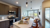 Located at 901 Nutt St in Wilmington, North Carolina, this modern single-floor residence offers a well-designed layout that balances comfort and contemporary style. The open-concept living and kitchen area serves as the heart of the home, where rich dark wood cabinetry pairs elegantly with white quartz countertops and a full suite of stainless steel appliances, including a refrigerator, electric range, and over-the-range microwave. A subway tile backsplash and pendant lighting above the kitchen island add refined character to the space. The living area receives generous natural light through large windows and a sliding glass door that opens to a private balcony, offering outdoor views of the surrounding Wilmington streetscape and greenery. Warm wood-look flooring flows continuously throughout, creating a cohesive and inviting atmosphere. The bedroom is a calm, well-proportioned retreat, accessible via a hallway and featuring window treatments that allow for adjustable natural light. The bathroom is appointed with a floating vanity, a full glass-enclosed walk-in shower with tile surround, and wood-look flooring that complements the rest of the residence. Clean lines, neutral tones, and thoughtful finishes define the overall aesthetic of this polished Wilmington address.