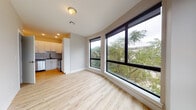 This thoughtfully designed single-floor unit offers a clean, contemporary aesthetic throughout. The open-concept living area is a standout feature, anchored by a striking bank of floor-to-ceiling black-framed windows that frame lush tree canopy views, flooding the space with natural light. Light-toned hardwood flooring runs throughout, lending warmth and visual continuity across every room.

The kitchen is efficiently laid out with white shaker cabinetry, a tile backsplash, a stainless steel refrigerator, dishwasher, and range, providing a functional and attractive workspace. Recessed lighting overhead ensures the kitchen remains bright and practical.

The bedroom is a calm, neutral space with the same hardwood flooring and ample wall space, offering flexibility in furnishing arrangements. Two doors provide access to additional rooms, supporting a connected and convenient layout.

The bathrooms are finished to a high standard, featuring marble-style tile in the shower surround and complementary grey floor tiles. A floating white vanity with brushed gold hardware and a well-placed vanity mirror complete the refined look.

A dedicated in-unit laundry area houses a stacked washer and dryer, adding everyday convenience. The entryway is clean and functional, providing a welcoming transition into the unit. Overall, the space presents a cohesive modern design with quality finishes throughout.