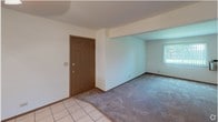 Located at 445 Donin Dr in Antioch, Illinois, this single-floor unit offers a practical and well-organized layout designed for comfortable everyday living. The kitchen is equipped with ample wood-toned cabinetry—both upper and lower—along with white appliances including a range, dishwasher, and refrigerator. Light tile flooring runs throughout the kitchen area, contributing to a clean and easy-to-maintain space. A mirrored wall accent adds a sense of depth to the kitchen. The layout transitions openly into a combined living and dining area, where neutral carpet provides warmth underfoot and a ceiling fan offers added comfort. The tiled entryway connects smoothly to the carpeted living space, creating a clear and inviting flow. A bedroom features plush carpeting and a large window fitted with vertical blinds, allowing natural light to filter in while maintaining privacy. Another bedroom includes dual doorways leading to a closet and an additional room, offering flexible storage options. The bathroom is finished with a full tub-shower combination, clean white fixtures, a wall-mounted mirror, and tile flooring, presenting a simple and functional design. Throughout the unit, neutral wall tones and wood trim details create a cohesive, understated aesthetic suited to a wide range of furnishing styles.