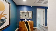 Located at 160 S Ventura Ave in Ventura, California, this thoughtfully designed single-floor residence showcases a cohesive and vibrant interior aesthetic that blends contemporary finishes with artisan character. The entry welcomes visitors with a striking deep-blue grasscloth accent wall, an organic live-edge wood console table with a dramatic resin inlay, and a colorfully framed mirror that sets a bold, creative tone.

The living area continues the deep-blue grasscloth wall treatment and features natural light from a garden-facing window. A curated gallery wall of framed artwork, a textured live-edge wood coffee table, and layered soft furnishings create a warm, inviting atmosphere.

The kitchen is outfitted with light wood cabinetry, open shelving, a white subway tile backsplash, and a full suite of stainless steel appliances, including a refrigerator, range, microwave, and dishwasher. Light wood-look flooring flows seamlessly throughout the space.

The bedroom is a calm retreat anchored by a warm golden grasscloth feature wall and a tall teal upholstered headboard. Mirrored closet doors and natural light from windows dressed in teal curtains enhance the room's depth and brightness.

The bathroom features teal accent walls paired with clean white tile, a soaking tub with shower combination, and warm wood-look flooring, completing the home's cohesive, coastal-inspired palette.