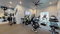 This modern fitness center is thoughtfully designed to accommodate a wide range of workout styles, all within a single, open-plan floor. The space is divided into distinct training zones that flow seamlessly into one another, creating an energetic yet organized environment.

The cardio area features a lineup of Matrix ellipticals, stair climbers, and treadmills positioned near a large window that offers views of an outdoor courtyard, allowing natural light to fill the space. A wall-mounted flat-screen TV provides entertainment during workouts.

At the heart of the facility, a bold turquoise turf lane — marked with yardage lines — runs the length of the room, ideal for sled pushes and functional training drills. A heavy-duty tire and TRX suspension systems complement this zone, while a vivid palm tree mural adds a dynamic visual backdrop.

The strength training section is generously stocked with Matrix selectorized machines, a full rack of dumbbells, medicine balls, and a power rack with punching bags. Floor-to-ceiling mirrors amplify the sense of space and support form-checking during lifts.

Throughout, large industrial-style ceiling fans maintain airflow, while recessed lighting keeps the atmosphere bright and motivating. Windows along multiple walls invite additional natural light, enhancing the overall open and functional ambiance of this well-appointed fitness facility.