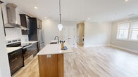 Located at 525 Ridge St, Unit 302 in Charlottesville, Virginia, this well-designed 2-bedroom, 2-bathroom residence offers a clean, contemporary aesthetic throughout. Light wood-tone flooring flows seamlessly across the entire unit, lending warmth and cohesion to each space.

The open-concept kitchen and living area serves as the heart of the home. The kitchen is a standout, featuring dark upper cabinetry, a patterned tile backsplash, stainless steel appliances, and a large center island with a light wood base and white quartz countertop. Globe pendant lights with matte black hardware add a modern touch, while a stainless range hood anchors the cooking area.

The living room is bright and open, with a large triple window fitted with roller shades that frame outdoor views of the surrounding Charlottesville neighborhood and greenery.

Both bedrooms are generously proportioned, filled with natural light from multiple windows, and finished with the same light wood flooring. The primary bedroom includes a ceiling fan and recessed lighting. The bathrooms are elegantly appointed — one features a floating wood vanity, white subway tile walk-in shower with glass enclosure, and warm brass lighting fixtures. The unit also includes an in-unit washer and dryer. Soft neutral paint tones throughout create a calm, move-in-ready atmosphere.