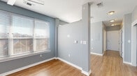 This single-floor residence offers a thoughtfully designed layout that balances functionality with modern aesthetics. Throughout the space, warm hardwood-style flooring provides a cohesive and inviting foundation, complemented by cool gray walls and crisp white trim and doors.

The kitchen is well-appointed with sleek, wood-toned cabinetry extending to the ceiling for generous storage, light-colored countertops, a double-basin sink, and a full suite of black appliances including a refrigerator, dishwasher, range, and over-the-range microwave. A large window floods the kitchen area with natural light.

The open living and dining areas benefit from multiple windows fitted with horizontal blinds, allowing for adjustable natural light throughout the day. Architectural column details add visual interest to the open-plan space. The bedroom is a comfortable retreat, featuring a ceiling fan, a sizable window with outdoor views, and ample room for furnishings.

The bathroom is finished with neutral tile flooring, a wood-toned vanity with a white countertop and integrated sink, a wall-mounted mirror, and chrome hardware accents. A central hallway connects all areas of the unit seamlessly, contributing to an efficient and practical floor plan.
