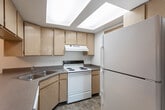 Located at 4516 S Triton Dr in Murray, Utah, this single-floor unit offers a practical and well-organized layout designed for comfortable everyday living. The living area is generously sized, featuring neutral-toned carpeting and crisp white walls that create a clean, bright atmosphere. A large sliding glass door dressed with vertical blinds fills the space with natural light and provides outdoor views. The layout flows naturally from the living area into adjacent spaces, including a functional kitchen equipped with light wood cabinetry, laminate countertops, a double-basin sink, a white electric range, a dishwasher, and a full-size refrigerator. Tile flooring in the kitchen adds durability and ease of maintenance. The bedrooms are carpeted and well-proportioned, each offering meaningful closet storage. One bedroom features a spacious walk-in closet with wire shelving, while another includes a double-door closet. The full bathroom is outfitted with a tub-shower combination, a vanity with a single sink and wood cabinetry, tile flooring, and convenient access to additional closet space. Throughout the unit, warm wood-toned doors complement the neutral color palette, contributing to a cohesive and understated aesthetic.