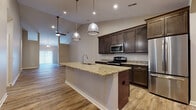 This single-story home is designed with an open-concept floor plan that seamlessly connects the living and kitchen areas beneath soaring vaulted ceilings. The expansive main living space is finished with wood-look plank flooring and ceiling fans, lending a clean, airy atmosphere throughout.

The kitchen serves as the centerpiece of the home, anchored by a large island with a granite countertop, undermount sink, and pendant lighting overhead. Dark espresso cabinetry lines the walls, complemented by granite countertops and a full suite of stainless steel appliances, including a range, microwave, dishwasher, and refrigerator. Arched doorways add an architectural detail that carries through the space.

The bedrooms are carpeted for comfort, with multiple windows providing natural light and ceiling fans for climate control. One bedroom connects directly to a hallway visible from the kitchen area.

The bathrooms feature wood-look tile flooring, dark espresso vanity cabinetry, and white countertops. The primary bathroom includes a dual-sink vanity and access to a walk-in closet with built-in shelving. A secondary bathroom offers a tub-shower combination with grab bars and a single-sink vanity.