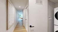 Located in the heart of downtown Montréal on Rue de la Montagne, this thoughtfully designed one-bedroom, one-bathroom unit makes excellent use of its compact footprint. The open-plan living area flows seamlessly from the kitchen to the sleeping quarters, unified by warm light hardwood flooring throughout.

The kitchen is both stylish and functional, featuring white cabinetry, light blue tile backsplash, stainless steel appliances including a full-size refrigerator, electric range, and built-in microwave. A peninsula with a white countertop and wood base doubles as a dining area with seating, maximizing the use of space.

The bedroom benefits from a large picture window with balcony access, inviting abundant natural light and views of lush greenery. Exposed concrete ceiling details lend an industrial character to the space, complemented by built-in white cabinetry for storage. The room also features a dedicated desk area, ideal for working from home.

The bathroom is clean and bright, finished in white tones with a glass-enclosed shower, built-in shelving, and patterned tile accents on the floor. A stacked washer and dryer unit is also included within the unit. Bold artwork and warm pendant lighting add personality, making this a well-appointed and efficient urban residence.