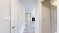 Located at 9807 Gable Ridge Terrace in Rockville, MD, this two-story home is thoughtfully laid out across two floors, with the more expansive main level housing the primary living areas and the upper level dedicated to the bedrooms. The living room is a standout space, distinguished by soaring vaulted ceilings, abundant natural light from large windows and sliding glass doors, and a wood-burning fireplace with a classic white mantle and dark surround. Light-toned hardwood-style flooring flows throughout the main level, lending a clean, cohesive aesthetic. The kitchen features white cabinetry, stainless steel appliances including a gas range and microwave, and a peninsula with a built-in sink and light stone countertops, opening conveniently to the living and dining areas. A hallway connects the main living spaces, maintaining an organized flow. Upstairs, the two bedrooms are carpeted and receive natural light through window treatments overlooking greenery. The primary bedroom includes a walk-in closet with wire shelving and direct access to an en-suite bathroom. Additional bathrooms feature tub-shower combinations with tiled surrounds and hardwood-style flooring. With four bathrooms total, the home offers substantial convenience across both floors.