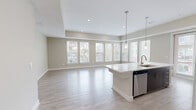 Located at 150 W Sam Houston Pkwy N in Houston, TX, this well-appointed 3-bedroom, 2-bathroom single-floor home offers a thoughtfully designed open-concept layout. The combined kitchen and living area is a standout feature, bathed in natural light from a sweeping bank of large windows that frame outdoor views of surrounding greenery. Light wood-look flooring flows throughout the main living spaces, complementing the neutral warm-beige color palette. The kitchen is equipped with stainless steel appliances, including a refrigerator, range, and microwave, alongside dark espresso cabinetry, a tile backsplash, and a central island with a white countertop and integrated sink. The spacious primary bedroom features plush carpeting and direct access to an en-suite bathroom. The bathrooms are finished with tile flooring, granite countertops, and a tiled tub-shower combination. Two closets provide ample storage, including a walk-in closet outfitted with built-in shelving and hanging rods. Additional bedrooms offer flexible space with light hardwood-style flooring. Recessed lighting and tray ceiling details add architectural dimension throughout the home, creating a clean, modern ambiance.