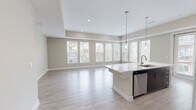 Located at 150 W Sam Houston Pkwy N in Houston, TX, this well-appointed 3-bedroom, 2-bathroom single-floor home offers a thoughtfully designed open-concept layout. The combined kitchen and living area is a standout feature, bathed in natural light from a sweeping bank of large windows that frame outdoor views of surrounding greenery. Light wood-look flooring flows throughout the main living spaces, complementing the neutral warm-beige color palette. The kitchen is equipped with stainless steel appliances, including a refrigerator, range, and microwave, alongside dark espresso cabinetry, a tile backsplash, and a central island with a white countertop and integrated sink. The spacious primary bedroom features plush carpeting and direct access to an en-suite bathroom. The bathrooms are finished with tile flooring, granite countertops, and a tiled tub-shower combination. Two closets provide ample storage, including a walk-in closet outfitted with built-in shelving and hanging rods. Additional bedrooms offer flexible space with light hardwood-style flooring. Recessed lighting and tray ceiling details add architectural dimension throughout the home, creating a clean, modern ambiance.