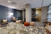 This 540 square foot space, located at 27 Barker Ave in White Plains, NY, presents a contemporary and thoughtfully designed communal area. The single-floor layout is divided into multiple seating zones, each with its own character. A standout feature is the striking marbled floor, which unifies the space with its abstract, earth-toned pattern. 

The room is illuminated by recessed lighting in a dropped ceiling, creating an even, ambient glow throughout. Large windows with sheer curtains allow natural light to flood the space, enhancing its open feel. 

Distinctive room dividers with intricate cutout patterns serve both functional and aesthetic purposes, delineating areas while maintaining an airy atmosphere. The furniture selection includes a mix of modern pieces - sleek sofas, minimalist chairs, and uniquely shaped ottomans in neutral tones with pops of orange for visual interest.

Artwork adorns the walls, adding sophistication and color to the neutral palette. A blue accent wall in one section provides depth and contrast. The space also includes thoughtful details like a floor lamp, side tables, and decorative elements, creating a balanced and inviting environment suitable for various communal activities.