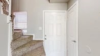 This two-story residence offers a thoughtfully organized layout spread across two floors, providing a clear separation between living and sleeping spaces. The ground floor houses the main living area, where the kitchen and living room flow together in an open arrangement. The kitchen is well-equipped with white cabinetry, granite-style countertops, a tile backsplash, wood-look flooring, and a window above the sink that brings in natural light. A pendant light adds a refined touch over the workspace. The living room features wood-look flooring, a ceiling fan with light kit, and a large sliding glass door dressed with vertical blinds, offering views of the surrounding neighborhood and filling the space with abundant natural light. A carpeted staircase leads to the upper floor, where the spacious primary bedroom is located. The bedroom features plush carpet, a ceiling fan, a window with blinds, and access to two separate doors — ideal for closet and entry separation. The bathroom presents a clean, modern aesthetic with white cabinetry, granite-style countertops, a single basin sink with brushed nickel fixtures, a large mirror, and wood-look flooring. Neutral tones and a textured ceiling are consistent throughout, giving the home a cohesive and understated character.