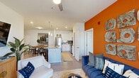 Located in Surf City, NC, this single-floor unit offers a thoughtfully designed open-concept layout that seamlessly connects the living, dining, and kitchen areas. The living room makes a bold statement with a striking orange accent wall, wood-look flooring, and sliding glass doors that open to a private balcony. The kitchen is well-appointed with white shaker cabinetry, granite countertops, a large island with an undermount sink, stainless steel appliances, a tile backsplash, and pendant lighting — plus a dedicated pantry with built-in shelving for added storage. A dining area nearby is accented by a framed vintage surf photography print, nodding to the coastal locale. The bedroom is a serene retreat highlighted by rich teal accent walls, a ceiling fan, and natural light from a large window. It connects to a generously sized walk-in closet with wire shelving. The bathroom features granite countertops, white cabinetry, and wood-look tile flooring. Throughout the space, curated coastal-inspired décor and vibrant color choices create a lively yet cohesive ambiance that reflects the spirit of Surf City living.