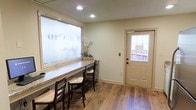 This single-floor Willow Creek Kennels space is designed with both functionality and comfort in mind. The reception and check-in area serves as the heart of the space, immediately welcoming visitors with warm, neutral-toned walls and rich hardwood-style flooring that lends a clean, grounded aesthetic throughout.

A long granite countertop runs along the front window, accompanied by ladder-back chairs with woven rush seats — creating a practical yet inviting workspace or client greeting area. The frosted front window features the Willow Creek Kennels branding, allowing diffused natural light to filter in while maintaining a professional appearance.

Recessed ceiling lighting supplements the natural light, ensuring the space remains bright and well-lit throughout the day. A panel door with a window insert provides access to an outdoor area, offering additional natural light and a view of the surrounding exterior deck or entryway.

The overall ambiance of the space is warm, clean, and professional — thoughtfully arranged to serve both staff and pet owners with ease. The cohesive use of neutral tones, natural materials, and practical furnishings reflects a space designed to be both welcoming and efficient for a kennel or pet care facility setting.