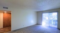 This single-floor residential space offers a clean and functional layout with a straightforward design. The living area features wall-to-wall carpeting in a neutral tone, providing a comfortable and cohesive foundation throughout the space. The walls are finished in a light, neutral color palette that contributes to a bright and open atmosphere. A textured popcorn ceiling adds a classic residential touch overhead. Natural light is a notable feature, streaming in through a sliding glass door fitted with vertical blinds, which offers both privacy control and access to the outdoors. The sliding door serves as the primary source of natural illumination, casting light across the carpeted floor and enhancing the airy feel of the room. The overall design is minimalist and move-in ready, offering a blank canvas for personalization. The space is well-suited for everyday living, with its simple finishes and practical layout making it an accessible and functional environment. The single-floor configuration ensures ease of movement throughout, making the space comfortable and straightforward to navigate.