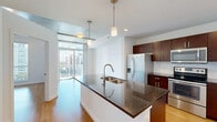 Located at 101 Lake Ave in downtown Orlando, this one-bedroom, one-bathroom residence offers a thoughtfully designed open-concept layout spread across a single floor. Light hardwood flooring flows throughout the main living areas, complementing the clean, modern aesthetic defined by crisp white walls and contemporary finishes.

The combined dining room, kitchen, and living area forms the heart of the home. The kitchen is outfitted with rich dark-wood cabinetry, granite countertops, a large center island with a dual-basin sink and pendant lighting overhead, and a full suite of stainless steel appliances including a refrigerator, range, microwave, and dishwasher. A subway tile backsplash adds a refined touch. Floor-to-ceiling windows and a glass door flood the living area with natural light while framing views of the Orlando skyline.

The bedroom is a comfortable, well-proportioned retreat featuring warm hardwood floors, an exposed concrete ceiling accent, a ceiling fan, and a large window overlooking the cityscape. Two closets provide generous storage. The bathroom features light tile flooring, a dark-wood vanity with a granite countertop, and clean, minimalist fixtures. Additional utility and laundry spaces round out this well-appointed urban residence.