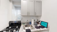 This well-appointed one-bedroom, one-bathroom unit offers a thoughtfully organized layout across a single floor. The living room serves as the central gathering space, showcasing warm parquet wood flooring laid in a classic basket-weave pattern that extends throughout the unit, lending a timeless character to the interior. Natural light enters through windows equipped with a wall-mounted air conditioning unit, complemented by a baseboard radiator for year-round climate control.

The kitchen is efficiently designed, featuring granite-style countertops, white shaker-style cabinetry, a stainless steel sink, and a gas range, providing all essential cooking amenities within a compact footprint. A window allows natural light into the space.

The bedroom is a comfortable, well-proportioned room with the same parquet flooring, a ceiling fan with light fixture, a window with an air conditioning unit, and access to a closet. A second closet provides additional storage elsewhere in the unit.

The bathroom includes a tub and shower combination with white tile surround and a vanity with matching cabinetry. Throughout the unit, white walls and clean lines create a bright, neutral ambiance.