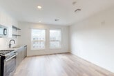 This thoughtfully designed studio in Everett, MA offers a clean, modern aesthetic throughout its well-utilized single-floor layout. Light wood-style flooring flows seamlessly across the open living area, creating a bright and cohesive feel enhanced by crisp white walls and recessed lighting overhead.

The kitchen is a standout feature, outfitted with stainless steel GE appliances including a gas range, built-in microwave, refrigerator, and dishwasher. Two-tone cabinetry in taupe and white, a subway tile backsplash, open floating shelves, and a undermount sink with a matte black faucet complete the contemporary look. Large windows in the kitchen and living area flood the space with natural light and provide open views of the surrounding neighborhood.

The living area is generously proportioned for a studio, offering ample room for flexible furniture arrangements. A hallway connects to the bathroom and two closets, providing practical storage solutions. The bathroom features stone-look tile flooring, a warm wood-toned vanity with gold hardware, and matte black accents, adding a refined touch to the space. Clean white walls and simple, modern fixtures maintain the studio's consistent aesthetic throughout.