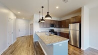 Located at 200 Jr Achievement Dr in Elkhart, Indiana, this single-floor residence offers a thoughtfully designed layout with contemporary finishes throughout. The kitchen is a standout feature, showcasing rich dark-stained cabinetry, granite countertops, a subway tile backsplash, and a full suite of stainless steel appliances including a gas range, microwave, refrigerator, and dishwasher. A center island with a granite surface and undermount sink provides additional prep space, illuminated by a trio of stylish industrial-style pendant lights. Wood-look plank flooring flows through the main living and kitchen areas, adding warmth and durability. The living area is bright and airy, featuring a ceiling fan and French doors that open to a private balcony, allowing abundant natural light and outdoor views. Bedrooms are finished with plush carpet and ceiling fans, offering a comfortable retreat. The bathroom is well-equipped with a granite-topped vanity, dark cabinetry, and a full tub-shower combination. A dedicated utility room houses a full-size side-by-side washer and dryer, adding everyday convenience. Neutral gray tones and clean white trim throughout lend the space a modern, cohesive aesthetic.