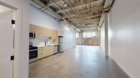 Located at 2349 S Santa Fe Ave in Los Angeles' vibrant Arts District, this single-floor loft-style space blends industrial character with modern updates. The open layout is defined by soaring ceilings with exposed reclaimed wood planks, raw structural beams, and visible conduit — all hallmarks of the building's warehouse origins. Polished concrete floors run throughout, providing a clean, durable foundation that complements the raw aesthetic.

The main open area is generously proportioned, offering a versatile canvas for living, working, or creative use. Exposed brick walls anchor one end of the space, accompanied by large multi-pane industrial windows that invite abundant natural light and lend an authentic loft character. An oversized ceiling fan enhances airflow across the expansive open floor plan.

The kitchen is thoughtfully appointed with light wood flat-front cabinetry, white quartz countertops, a stainless steel sink with a matte black faucet, and a full suite of stainless steel appliances including a gas range, microwave, and dishwasher. A clean white tile backsplash ties the modern finishes together seamlessly.

The bathroom features floor-to-ceiling white subway tile, a soaking tub with shower combination, and matte black fixtures for a refined, contemporary contrast. A secondary room with white walls and exposed ceiling details offers flexible use as a bedroom, studio, or office.