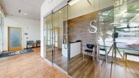 Located at 3020 University Ave SE in Minneapolis, MN, this fitness center and lobby occupies a single floor with a thoughtfully designed layout that includes a dedicated exercise room and a connecting hallway. The lobby entrance greets visitors with warm tile flooring, floor-to-ceiling glass partitions, and a sleek reception area accented by a wood-panel feature wall and modern branding signage. Natural light streams in through large windows and glass doors, creating a bright and welcoming atmosphere. The hallway connecting the lobby to the fitness area features clean white walls, recessed lighting, and additional seating for guests. The exercise room is generously sized and well-appointed, offering a comprehensive range of fitness equipment including treadmills, ellipticals, a stationary bike, a multi-function cable machine, a weight bench, dumbbells, medicine balls, and kettlebells. Distinctive circular ceiling panels and pendant lighting give the fitness area a modern, polished aesthetic, while large windows along the exterior walls allow abundant natural light and views of the surrounding neighborhood. Durable rubber flooring throughout the exercise room ensures both safety and functionality. Together, the spaces deliver a professional and energizing environment suited for a full fitness experience.
