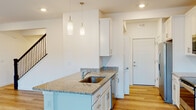 This well-designed two-story home offers a clean, contemporary aesthetic throughout its thoughtfully arranged layout. The kitchen serves as a central highlight, showcasing crisp white shaker-style cabinetry, granite countertops, and a full suite of stainless steel appliances including a refrigerator, electric range, microwave, and dishwasher. A peninsula with an undermount sink and pendant lighting above adds both functionality and style, while light hardwood flooring ties the kitchen and adjacent living areas together seamlessly. Sliding glass doors at the far end of the kitchen invite natural light and provide outdoor access. The entry area flows naturally from the kitchen, featuring a clean white front door and direct sightlines through the space. Upstairs, the bedrooms are finished with plush carpet and feature windows that allow ample natural light, with ceiling fans providing additional comfort. The bathrooms are finished in a consistent palette of white cabinetry, granite-topped vanities, large mirrors, and tub-shower combinations, maintaining the home's cohesive modern style. Throughout, recessed lighting, neutral white walls, and quality finishes create a bright, move-in-ready environment that is both functional and visually inviting.