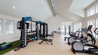 Located at 4550 Atrium Ct in Wilmington, NC, this single-floor fitness facility is thoughtfully designed to accommodate a full range of training disciplines. The space is defined by soaring vaulted ceilings with recessed lighting and exposed ductwork that lends an industrial-chic aesthetic, all set against crisp white walls and light hardwood-style flooring that creates a bright, energizing atmosphere.

The strength training zone is anchored by a robust power rack system outfitted with a comprehensive dumbbell rack, kettlebells, medicine balls, and adjustable benches, providing everything needed for a complete resistance workout. Adjacent to this area, a dedicated turf section with artificial grass supports functional training activities, featuring a tire flip station, agility cones, plyo boxes, and a wall-mounted flat-screen TV for guided programming.

The cardio zone is generously stocked with multiple treadmills, elliptical machines, and stationary bikes — including a spin bike — all positioned near large windows that frame views of the outdoor pool area, filling the space with natural light and visual connection to the outdoors. A cable machine and additional free weight stations round out the strength offerings. Practical amenities include a wall-mounted water fountain station, ensuring convenience during intense sessions. The facility's open floor plan and high ceilings create a spacious, motivating environment suited to individual and group training alike.
