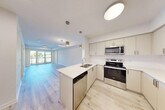 Located at 1475 Whites Rd in Pickering, Ontario, this well-appointed one-bedroom, one-bathroom unit offers a thoughtfully designed layout across a single floor. Light-toned hardwood flooring runs throughout the living spaces, lending a clean, modern aesthetic that enhances the sense of openness.

The kitchen is a standout feature, finished with crisp white cabinetry, a bright countertop with an integrated sink, and a full suite of stainless steel appliances including a refrigerator, electric range, and over-the-range microwave. Pendant lighting overhead adds a contemporary finishing touch.

The open living area is bathed in natural light, courtesy of a large sliding glass door that leads to a balcony overlooking the green surroundings of the neighbourhood. A circular pendant light fixture anchors the space with a modern design element.

The bedroom is a comfortable and well-proportioned room featuring light hardwood floors, a mirrored sliding closet, and a window with views of the adjacent residential development. The four-piece bathroom includes a combined shower and soaker tub with clean white finishes and tile flooring.

Completing the unit is a dedicated in-suite laundry room equipped with a full-sized top-load washer and dryer, offering everyday convenience.