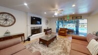 Located at 39900 Blacow Rd in Fremont, California, this single-floor community space is thoughtfully designed to accommodate gatherings and everyday use. The open-plan layout seamlessly connects the living room, dining area, and kitchen, creating a cohesive and welcoming environment throughout.

The living room is a standout feature, anchored by a white-painted brick fireplace with a decorative iron screen and a wall-mounted flat-screen television above. Comfortable seating is arranged around a plush area rug and a wood-top coffee table, while ceiling fans with integrated lighting ensure year-round comfort. Recessed lighting throughout adds a warm, even glow to the space.

Light wood-look flooring runs continuously across the entire floor, contributing to a clean and unified aesthetic. Large sliding glass doors flood the living area with natural light and provide direct access to an outdoor pool area, offering inviting views of the exterior amenity space.

The dining area features a substantial bar-height table with cross-back chairs, positioned adjacent to the kitchen. The kitchen itself includes a bar-style counter with seating, a stainless steel refrigerator, microwave, and light wood cabinetry for storage.

Two bathrooms serve the space, each finished with wood-look flooring, neutral tones, and functional fixtures. A hallway and two closets provide additional utility and storage, completing this well-appointed and versatile community space.