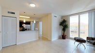 This well-appointed single-floor residence offers a clean, modern aesthetic throughout, with light-toned ceramic tile flooring connecting each room seamlessly. The open-concept living area is bathed in natural light, anchored by a sliding glass door that leads to a private balcony overlooking lush palm trees and the surrounding neighborhood, creating an airy, tropical ambiance.

The kitchen is a standout feature, showcasing rich dark cabinetry that contrasts beautifully with granite countertops and a full suite of stainless steel appliances, including a French door refrigerator, electric range with microwave, and dishwasher. Pendant lighting above the kitchen bar adds a stylish finishing touch.

Two well-sized bedrooms offer neutral walls and generous windows that invite ample natural light. One bedroom includes access to a spacious walk-in closet outfitted with wire shelving for organized storage.

Both bathrooms mirror the home's contemporary design with dark vanity cabinetry, white countertops, large mirrors, and tiled tub-shower combinations. The consistent use of light, neutral tones throughout the space contributes to a calm and welcoming atmosphere, making this residence both functional and visually cohesive.