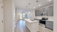 Located at 510 McLean St in Belmont, NC, this well-appointed one-bedroom, one-bathroom residence offers a thoughtfully designed single-level layout with modern finishes throughout. The open-concept living and kitchen area serves as the heart of the home, anchored by a central island with a white quartz countertop and an undermount sink, illuminated by stylish pendant lighting. The kitchen is outfitted with gray shaker-style cabinetry, stainless steel appliances including a range, microwave, and refrigerator, all set against light wood-look luxury vinyl plank flooring that flows seamlessly through the space. Natural light enters through a glass-paned entry door at the end of the living area, enhancing the bright, airy atmosphere complemented by recessed lighting overhead. The bedroom is a comfortable retreat featuring a ceiling fan, a window with exterior views, and built-in wall shelving for added storage and display. A dedicated closet provides additional organization. The full bathroom features matching gray cabinetry with a white countertop, a large mirror, a glass-enclosed shower, and consistent wood-look flooring that ties the space together. Clean white walls and crisp trim finishes lend a fresh, contemporary feel throughout this move-in-ready residence.