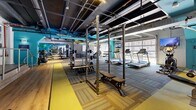 Located at 800 N Pennsylvania St in Denver, Colorado, this fitness center offers a generously sized, single-level exercise space designed to accommodate a comprehensive range of workout styles. The industrial-inspired interior features exposed ductwork and piping along the dark ceiling, lending the facility a modern, urban aesthetic complemented by bold accent walls in teal, olive green, and yellow.

The layout is thoughtfully organized to separate functional training zones. A dedicated free weights area includes a full dumbbell rack and multiple adjustable benches, while a strength training section features heavy-duty power racks and barbell stations suitable for serious lifters. Cardio equipment, including a row of treadmills positioned along windowed walls, provides natural light and street views during workouts.

Open floor space is covered with large rubber fitness mats and hardwood-style flooring, offering ample room for stretching, functional training, and dynamic movements. Additional equipment such as a punching bag, stability balls, and cable machines rounds out the facility's versatility. Wall-mounted mirrors enhance the sense of space and support form monitoring throughout. Motivational artwork and signage contribute to the energetic atmosphere, making this a well-equipped and visually engaging fitness destination in the heart of Denver.
