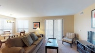 This single-floor residence offers a thoughtfully designed layout that balances comfort and functionality across its key living areas. The living room serves as the central gathering space, featuring warm neutral-toned walls, plush carpeting, and a large sliding glass door dressed with vertical blinds that fills the room with natural light and provides outdoor access. The space comfortably accommodates a full sofa ensemble, accent seating, and an entertainment center. Adjacent to the living area, a dedicated dining nook features corner windows with horizontal blinds, allowing additional natural light to brighten the space around a glass-top table. The kitchen is well-equipped with honey-toned wood cabinetry, granite-style countertops, tile flooring, and stainless steel appliances including a range with over-the-range microwave. The bedroom is generously sized with soft carpeting, mirrored sliding closet doors, a substantial dark-wood dresser with mirror, and coordinating nightstands. Two bathrooms complete the unit: a spacious primary bath featuring large-format tile flooring, a granite-topped vanity, and a glass-enclosed shower, and a second full bath with a tub/shower combination and an extended granite vanity. Warm, neutral tones and consistent finishes tie the entire space together cohesively.