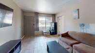 Located at 13031 Central Ave NE in Albuquerque, New Mexico, this one-bedroom, three-bathroom unit offers a thoughtfully organized single-floor layout that maximizes every square foot of available space. The living room features wood-look tile flooring, a wall-mounted television, a sliding window that invites natural light, and a wall-unit air conditioner for year-round comfort. A front entry door with a keypad lock adds a layer of security and convenience. The compact kitchen is efficiently designed with warm honey-toned cabinetry, granite-style countertops, a stainless steel refrigerator, an electric cooktop, an over-the-range microwave, and a sink — providing all essential appliances within a well-organized footprint. The spacious bedroom features plush carpeting, wall sconce lighting, a sliding window with curtains, and a dedicated closet area with built-in shelving and hanging rods. A versatile carpeted area adjacent to the bedroom functions well as a home office or additional living space. Three bathrooms include tiled tub-shower combinations with safety grab bars, vanity mirrors, and tile flooring, offering practical and accessible design throughout. The unit presents a functional, no-frills living environment well-suited for everyday comfort.