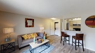 This single-floor residence offers a thoughtfully organized layout across several well-defined spaces. The living room serves as the heart of the unit, featuring warm-toned wood-style flooring, neutral walls, and a textured ceiling. A bar-height counter with woven rattan seating creates a natural transition into the kitchen, allowing for an open, connected feel between the two spaces. Windows provide natural light, contributing to the room's welcoming ambiance.

The kitchen is efficiently designed with a galley-style layout, featuring taupe cabinetry with sleek hardware, white countertops, and black appliances including an electric range and refrigerator. A multi-bulb ceiling fixture provides ample task lighting throughout the space. Notably, an in-unit stacked washer and dryer is tucked into a dedicated closet just off the living area, adding practical convenience.

The bedroom offers plush wall-to-wall carpeting and a large sliding-door closet with a full rod and shelving for generous storage. A textured ceiling and neutral walls maintain the consistent, calm aesthetic found throughout the unit.

The bathroom features a full-size soaking tub with an overhead shower, clean white surrounds, and chrome fixtures, offering a simple and functional design.