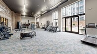 This state-of-the-art fitness center, located at 500 W 14th St in Richmond, VA, offers a spacious 1,840 square feet of cutting-edge exercise space. The facility boasts a harmonious blend of industrial and modern design elements, featuring exposed brick walls that add character and warmth to the space. High ceilings with suspended LED lighting create an open, airy atmosphere, while large windows allow abundant natural light to flood the area.

The gym is equipped with a comprehensive range of fitness equipment, including cardio machines like treadmills and ellipticals, as well as strength training apparatus such as weight machines and free weights. The layout is thoughtfully designed to accommodate various workout styles and preferences, with dedicated areas for different exercise routines.

Notable features include multiple flatscreen TVs for entertainment, motivational wall art, and a climbing wall for added variety in workout options. The facility's modern flooring combines durability with aesthetic appeal, complementing the overall design scheme. With its spacious layout and diverse equipment selection, this fitness center caters to exercise enthusiasts of all levels, providing an inviting and functional environment for achieving health and wellness goals.