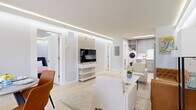 This thoughtfully designed single-floor unit offers three bedrooms and two bathrooms within a compact, efficiently laid-out floor plan. The open-concept living and dining area serves as the heart of the space, featuring light hardwood-style flooring, a coffered ceiling with elegant recessed LED strip lighting, and large windows with direct access to an outdoor area, allowing natural light to fill the room. A marble-top coffee table and mixed seating anchor the living zone, while a dedicated dining area accommodates a small table and chairs.

The kitchen is fitted with gray shaker-style cabinetry, white subway tile backsplash, white quartz countertops, and a full suite of stainless steel appliances including a refrigerator, electric range, microwave, and dishwasher. A stacked washer and dryer unit is integrated into the kitchen area for added convenience.

Each bedroom features the same recessed LED cove lighting and light flooring, with the primary bedroom offering a mirrored sliding-door closet. The bathrooms are finished with marble-style tile, a frameless glass shower enclosure with black hardware, and gray vanity cabinetry, reflecting a clean, contemporary aesthetic throughout.
