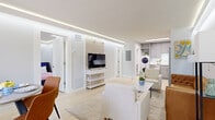 This thoughtfully designed single-floor unit offers three bedrooms and two bathrooms within a compact, efficiently laid-out floor plan. The open-concept living and dining area serves as the heart of the space, featuring light hardwood-style flooring, a coffered ceiling with elegant recessed LED strip lighting, and large windows with direct access to an outdoor area, allowing natural light to fill the room. A marble-top coffee table and mixed seating anchor the living zone, while a dedicated dining area accommodates a small table and chairs.

The kitchen is fitted with gray shaker-style cabinetry, white subway tile backsplash, white quartz countertops, and a full suite of stainless steel appliances including a refrigerator, electric range, microwave, and dishwasher. A stacked washer and dryer unit is integrated into the kitchen area for added convenience.

Each bedroom features the same recessed LED cove lighting and light flooring, with the primary bedroom offering a mirrored sliding-door closet. The bathrooms are finished with marble-style tile, a frameless glass shower enclosure with black hardware, and gray vanity cabinetry, reflecting a clean, contemporary aesthetic throughout.