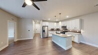 Located in Austin's vibrant 78702 zip code, this well-appointed single-story home offers a thoughtfully designed open-concept layout. The combined kitchen and living area serves as the heart of the home, featuring rich wood-look flooring, recessed lighting, and a ceiling fan that keeps the space comfortable year-round. The kitchen is a standout, showcasing crisp white shaker cabinets with matte black hardware, a neutral tile backsplash, quartz countertops, a central island with an undermount sink, and a full suite of stainless steel appliances. Natural light pours into the living room through tall windows and a glass-paneled door that opens to an outdoor area. A clean hallway connects the main living space to the private quarters. Both bedrooms are carpeted for warmth and comfort, with ceiling fans and windows that invite natural light. One bedroom features built-in open shelving, adding practical storage and display space. The full bathroom is finished with white vertical subway tile in the tub/shower surround, matte black fixtures, a white vanity, and a large mirror framed in black. A dedicated closet completes the functional layout of this clean, modern Austin home.