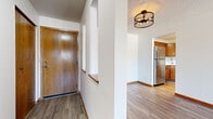 This single-floor unit offers a practical and well-organized layout across a comfortable footprint. The entryway greets residents with warm wood-toned flooring and a distinctive structural column featuring built-in display niches, adding architectural character to the transition space. An industrial-style cage flush-mount light fixture overhead enhances the entry's visual appeal.

The kitchen and living room share an open-plan arrangement, promoting a connected, functional flow. The kitchen is equipped with warm oak cabinetry providing ample upper and lower storage, light-toned countertops, a stainless steel double-basin sink, and a stainless steel refrigerator. The adjoining living area features plush carpet and a textured ceiling, with a clear sightline into the kitchen.

Both bedrooms are carpeted and finished with clean white walls and wood baseboards. The primary bedroom is a generous size, complemented by a spacious walk-in closet featuring wire shelving for organized storage. A second closet serves the additional bedroom. Windows in the bedrooms allow for natural light.

The three bathrooms are finished in a clean, neutral palette, with oak vanities, light countertops, white tile flooring, and tub-shower combinations, maintaining a consistent and tidy aesthetic throughout.