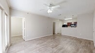 This thoughtfully designed single-floor residence offers a comfortable and functional layout across a well-utilized footprint. Light-toned wood-look flooring runs throughout the main living areas, creating a clean and cohesive aesthetic, while neutral warm-gray walls provide a versatile backdrop throughout.

The open-concept living room is bright and airy, featuring crown molding, a ceiling fan with light fixture, and a set of French doors that lead to a private balcony, allowing natural light to fill the space. The kitchen is positioned adjacent to the living area and features rich dark-wood cabinetry, light stone-look countertops, a peninsula breakfast bar with pendant lighting, and a full suite of black appliances including a refrigerator, electric range, and microwave.

The bedroom offers a comfortable, carpeted retreat with its own ceiling fan and a window providing natural light. A dedicated office space adds flexibility for remote work or study. The full bathroom includes a dark-wood vanity with a stone-look countertop, a full soaking tub and shower combination, and matching wood-look flooring. Additional conveniences include a hallway, a closet for storage, and an in-unit laundry area, making this residence both practical and inviting.